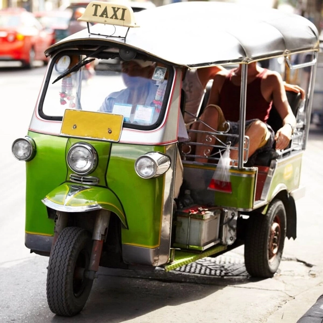 Un tuk-tuk taxi circule dans la rue, offrant un moyen de transport unique et coloré dans un environnement urbain animé.