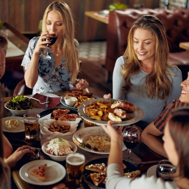 The image shows a group of individuals seated around a table filled with various dishes, suggesting a social dining scenario. The faces of the individuals are obscured by brown rectangles, maintaining privacy and focusing attention on the communal aspect of the meal. 