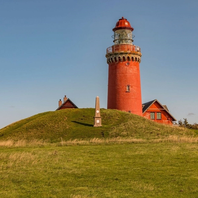 Un phare rouge perché sur une colline, se dressant majestueusement contre le ciel bleu.