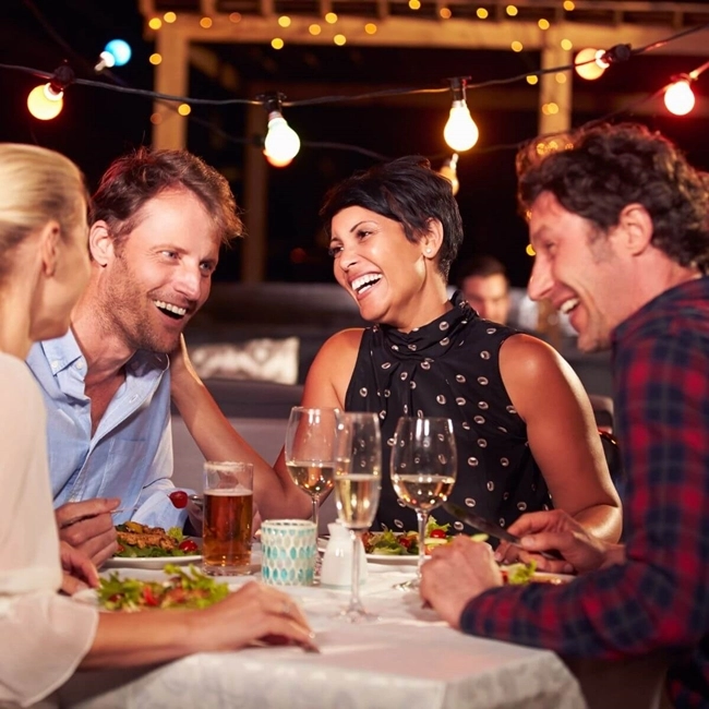 Un groupe de personnes assises autour d'une table, partageant des boissons et des plats variés dans une ambiance conviviale.