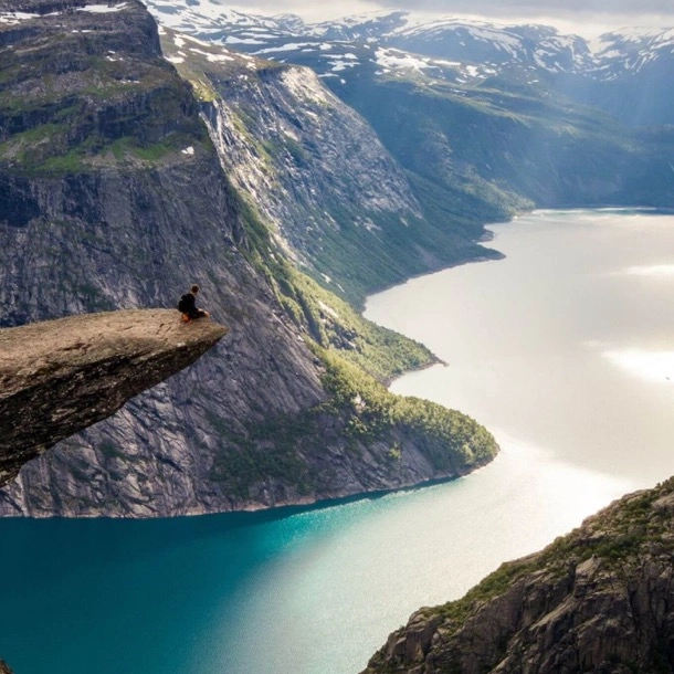 A person sitting atop a cliff, contemplating a peaceful lake below.