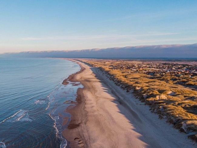 Vue aérienne d'une plage avec des dunes de sable, mettant en valeur la beauté naturelle du littoral.